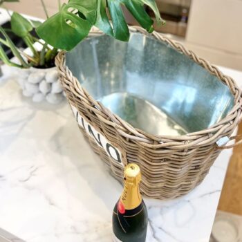 Kubu Vino Cooler Basket with a bottle of champagne next to it on a white marble surface